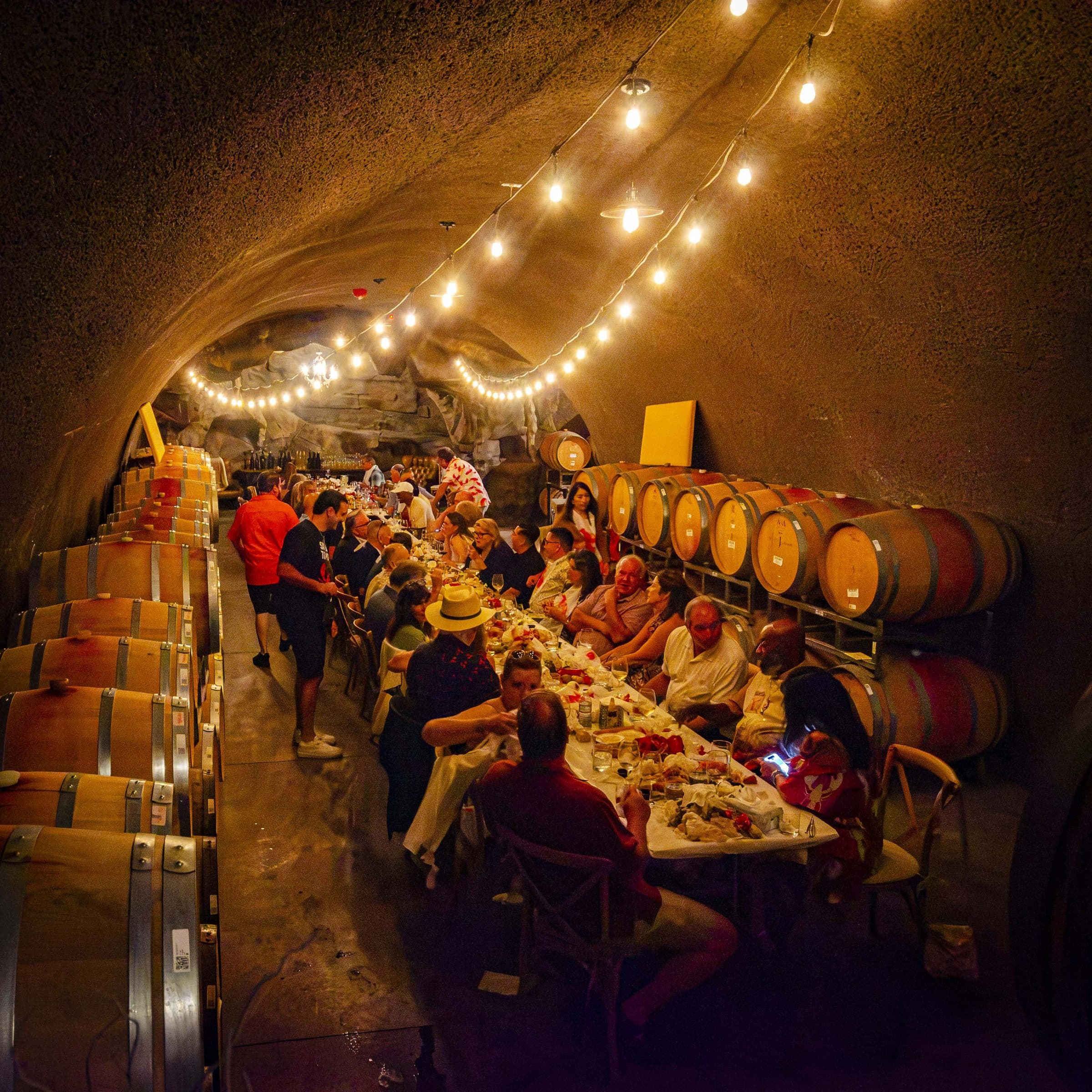 Guests at a long dinner table under string lights in the Joseph Cellars wine cave